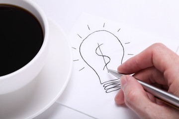 Light bulb with a dollar sign drawn with a pen on a napkin next to a coffee cup