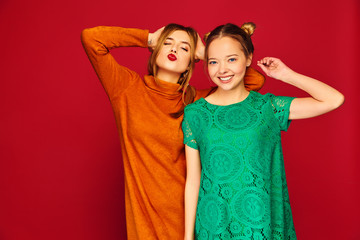 Two young beautiful blond smiling hipster girls posing in trendy summer clothes. Carefree women isolated on red background. Positive models going crazy and hugging