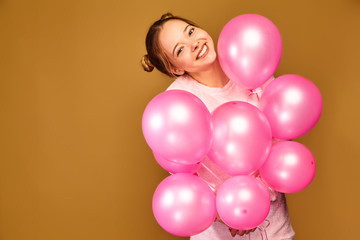 Fototapeta na wymiar Excited young girl in white cute clothes. Woman model with pink air balloons on golden background. St. Women's Day; Happy New Year; birthday holiday party