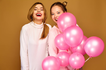 Fototapeta na wymiar Two excited young girls in white cute clothes. Women models with pink air balloons on golden background. St. Women's Day; Happy New Year; birthday holiday party