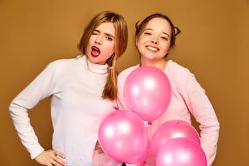 Two excited young girls in white cute clothes. Women models with pink air balloons on golden background. St. Women's Day; Happy New Year; birthday holiday party