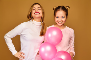 Two excited young girls in white cute clothes. Women models with pink air balloons on golden background. St. Women's Day; Happy New Year; birthday holiday party