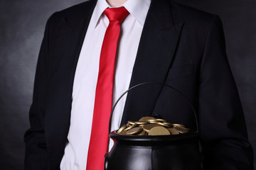 A man wearing a black suit is holding a pot of gold