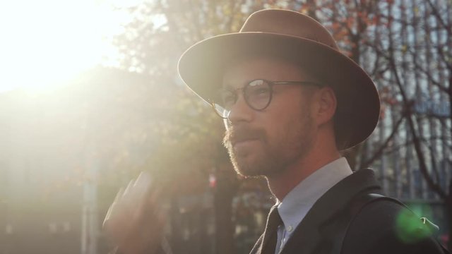 Stylish hipster man in hat and glasses in sun glare at autumn street