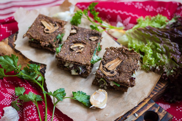 Crispy rye and flax seeds breads dehydrated and stuffed with fresh green salad leaves, mushrooms and Arabian hummus spread paste. Vegan, vegetarian snack on Christmas red tablecloth background.
