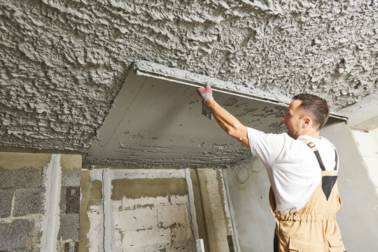 Plasterer smoothing plaster mortar on ceiling with screeder