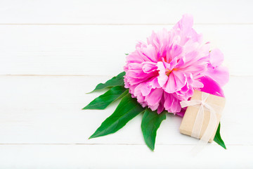 Small gift with pink peony on white wooden background