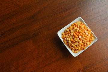 White bowl with grains of yellow dried peas on a wooden table, top view. Photo with empty place for text.   