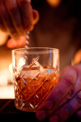 Expert barman is making cocktail at night club. Professional bartender at work in bar pouring sweet drink into glass on party at night club. Barman is decorating cocktail.