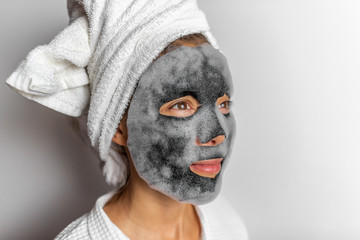 Face mask foam bubbles charcoal detox facial treatment at home -asian girl purifying skin removing dead skin cells with chemical peel korean face sheet in bathroom.