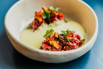 Meat tartare with mushrooms, sauce and greenery on a white plate