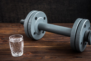 Obraz na płótnie Canvas Glass of vodka and dumbbell on wooden background. Sport and alcohol concept.