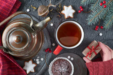 Xmas background with tea, sweets and female hand holding small gift box