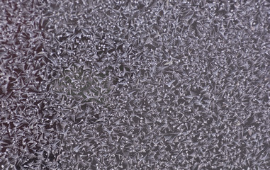 Snowflakes on window glass in winter blue texture on window. Abstract icy festive background. Close-up. Soft focus