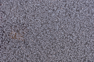 Frost patterns on window glass in winter. Abstract icy festive background. Close-up. Soft focus