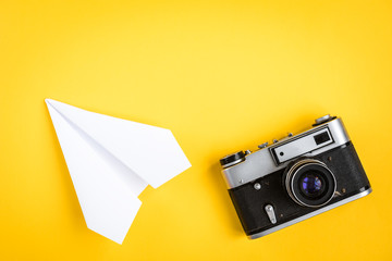 Old camera and paper plane on yellow background.