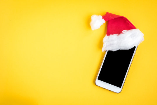 Mobile phone with Christmas hat on yellow background.