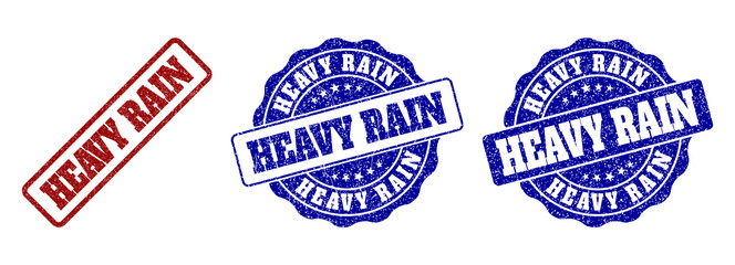HEAVY RAIN scratched stamp seals in red and blue colors. Vector HEAVY RAIN labels with distress style. Graphic elements are rounded rectangles, rosettes, circles and text titles.