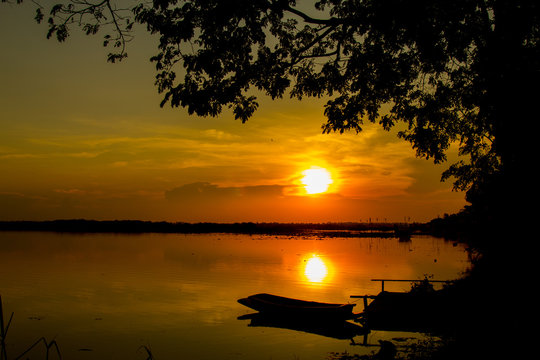 Silhouette shot,  Sunset with boat  and tree over lake or pond or swamp of Bueng See Fai, Phichit, Thailand.
