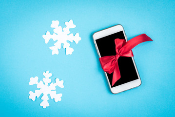 Mobile phone with red bow and paper snowflakes on blue background.