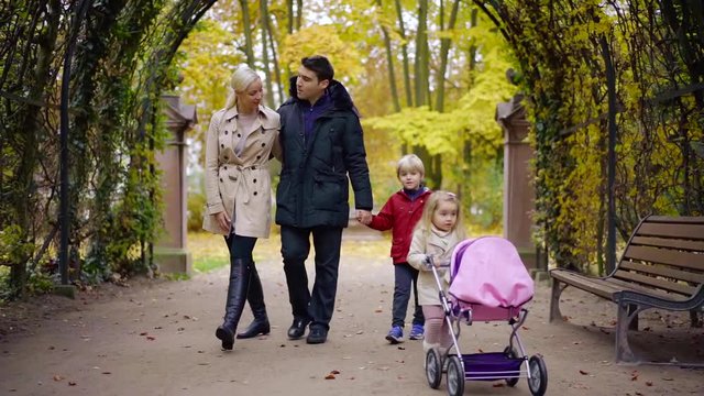 parents with their little son and daughter are walking in autumn park, man and woman are embracing