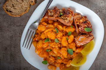 Beans stew with pork ribs and pickles on a white plate