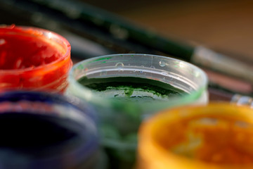 several jars of colored gouache stand in the sun on the background of the brush