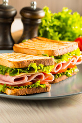 Close-up of two sandwiches with bacon, salami, prosciutto and fresh vegetables on rustic wooden cutting board. Club sandwich concept.