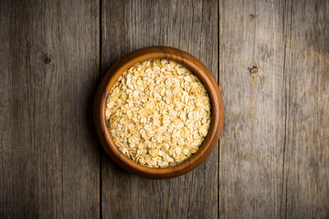 Wooden bowl with uncooked oats on the rustic wooden background. Selective focus. Shallow depth of field.
