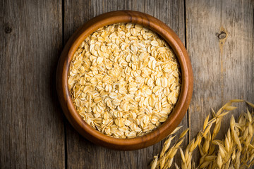 Wooden bowl with uncooked oats on the rustic wooden background. Selective focus. Shallow depth of field.
