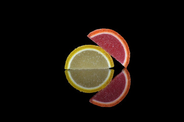 Two marmalade multi-colored slices on a black background with symmetrical reflection in the glass