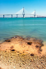 PUENTE EN LA BAHÍA DE CÁDIZ Y ORILLA CON ROCAS