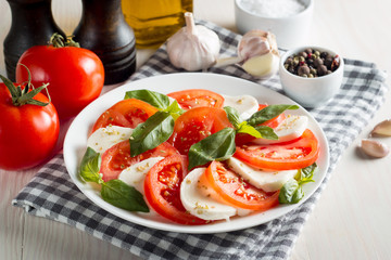 Photo of Caprese Salad with tomatoes, basil, mozzarella, olives and olive oil on wooden background. Italian traditional caprese salad ingredients. Mediterranean, organic and natural food concept.