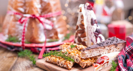 Traditional Italian Christmas fruit cake Panettone Pandoro with festive red ribbon and sweets from nuts and nougat. On a wooden background. Free space for text.