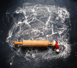 Christmas Baking background. Rolling pin in christmas hat with flour on a dark background