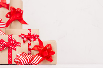 Holiday decoration composition of gift boxes with traditional red ribbons and bows on soft white wood board, copy space, closeup.