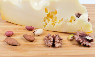 Piece of maasdam cheese among of various nuts close-up