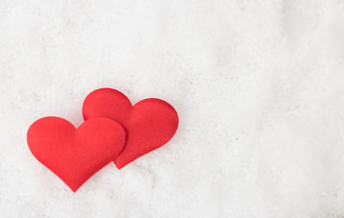 Two decorative red hearts are on white snow background with copy space for message.