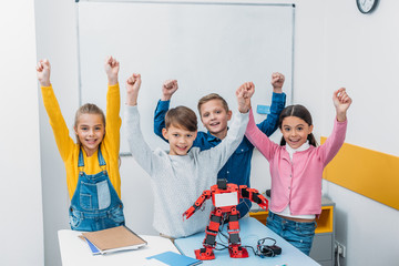happy schoolchildren raising hands, smiling and looking at camera in stem class © LIGHTFIELD STUDIOS