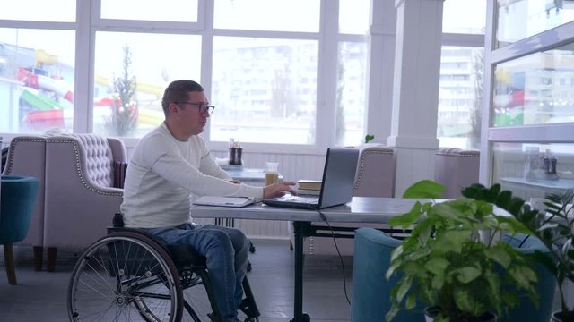 online payment, happy disabled into glasses in wheelchair with plastic card does internet purchases using modern computer technology during during freelance work in restaurant