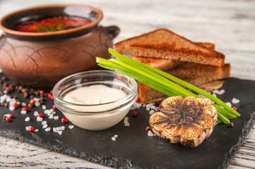 Ukrainian national dish borscht. Red Russian borsch in a clay pot with onions, sauce, sour cream, bread croutons, roasted garlic