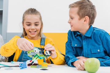 Obraz premium happy schoolchildren making robot with details in classroom