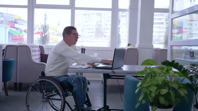online shopping, invalid spectacles in wheelchair with credit card makes payment in Internet using smart computer technology during remote business management in cafe