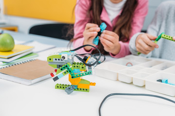 cropped view of classmates working together on project during STEM lesson with handmade robot model...