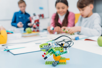multicolored handmade robot at desk with schoolchildren at background in stem class
