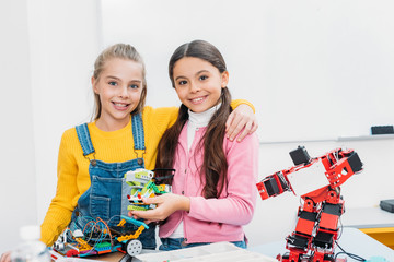 smiling schoolgirls holding robot and looking at camera in stem class