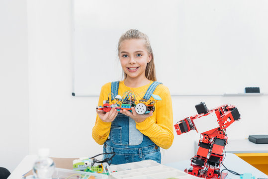 smiling schoolgirl looking at camera and presenting handmade robot model at STEM lesson