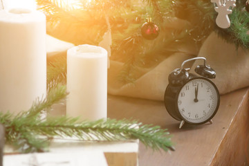 Black alarm clock on wooden table on background of Christmas tree. Sun shining orange toned. New Year Theme