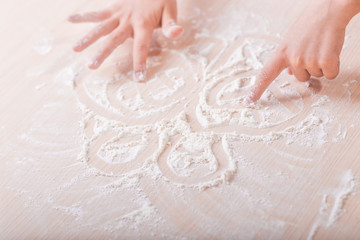 Obraz premium children's hands draw patterns of white flour on the table. baking preparation stage. little game
