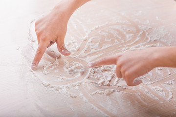 Fototapeta premium children's hands draw patterns of white flour on the table. baking preparation stage. little game
